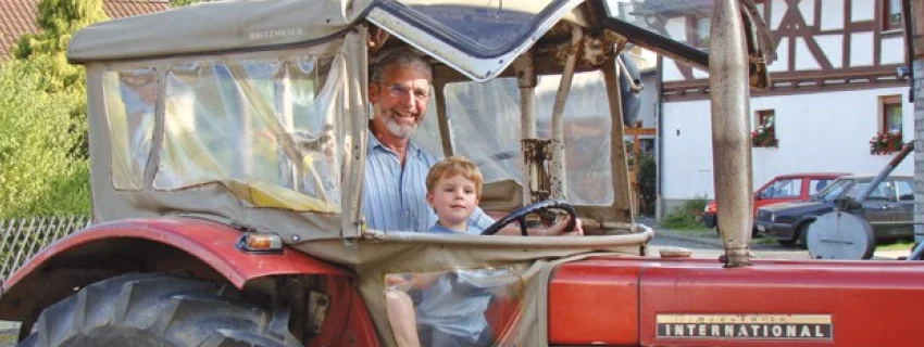 Ein Mann und ein Kind sitzen in einem Roten Traktor am Lenkrad.