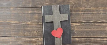 Auf einem, in Leder gebundenem, Buch liegt ein Holzkreuz und ein Herz.