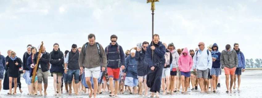 Eine Gruppe von Menschen läuft über den Strand auf den Beobachter zu. Sie tragen ein Kreuz.