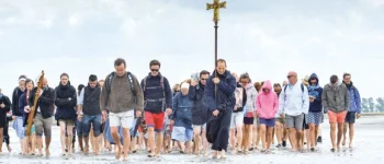 Eine Gruppe von Menschen läuft über den Strand auf den Beobachter zu. Sie tragen ein Kreuz.