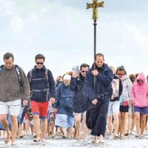 Eine Gruppe von Menschen läuft über den Strand auf den Beobachter zu. Sie tragen ein Kreuz.