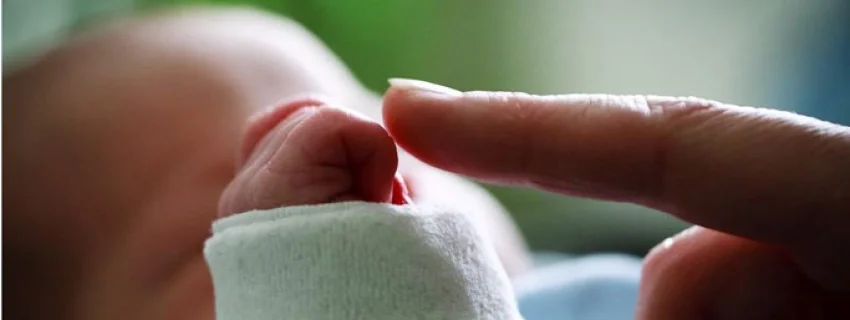 ein Zeigefinger berührt die Hand eines Babys