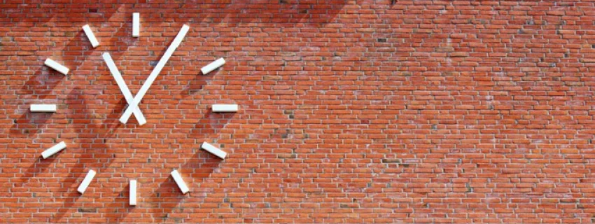 Wie spät ist es in meinem Leben? Aufmerken. durchatmen. ausrichten. weitergehen. Bild einer Uhr an einer Ziegelsteinwand.