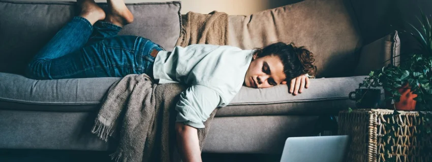 Frau liegt erschöpft auf einem Sofa, eine Hand am Laptop