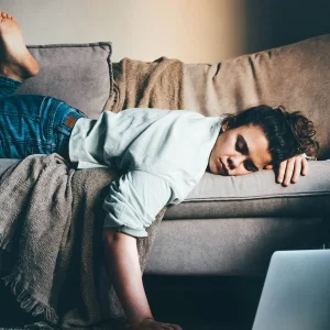 Frau liegt erschöpft auf einem Sofa, eine Hand am Laptop